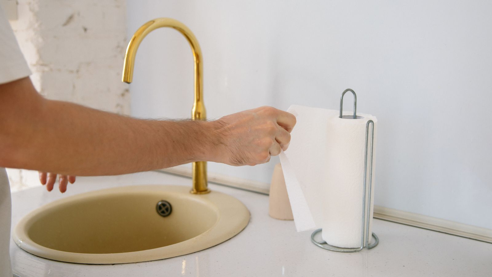 Hand pulling a sheet from a paper towel roll near a kitchen sink