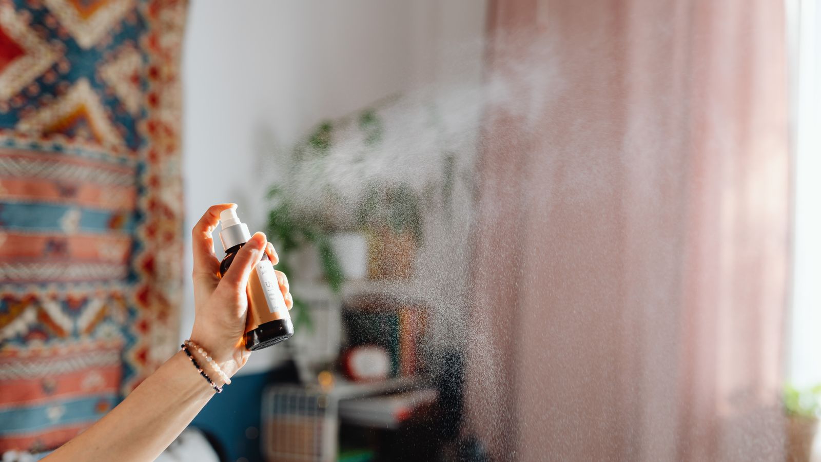 Bottle of fabric refresher spray being used on fabric at home