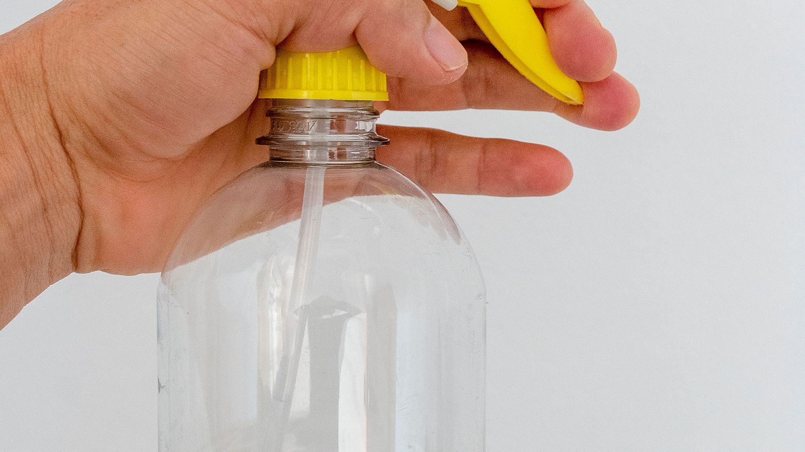 Hand holding a clear fabric refresher spray bottle checking the liquid inside