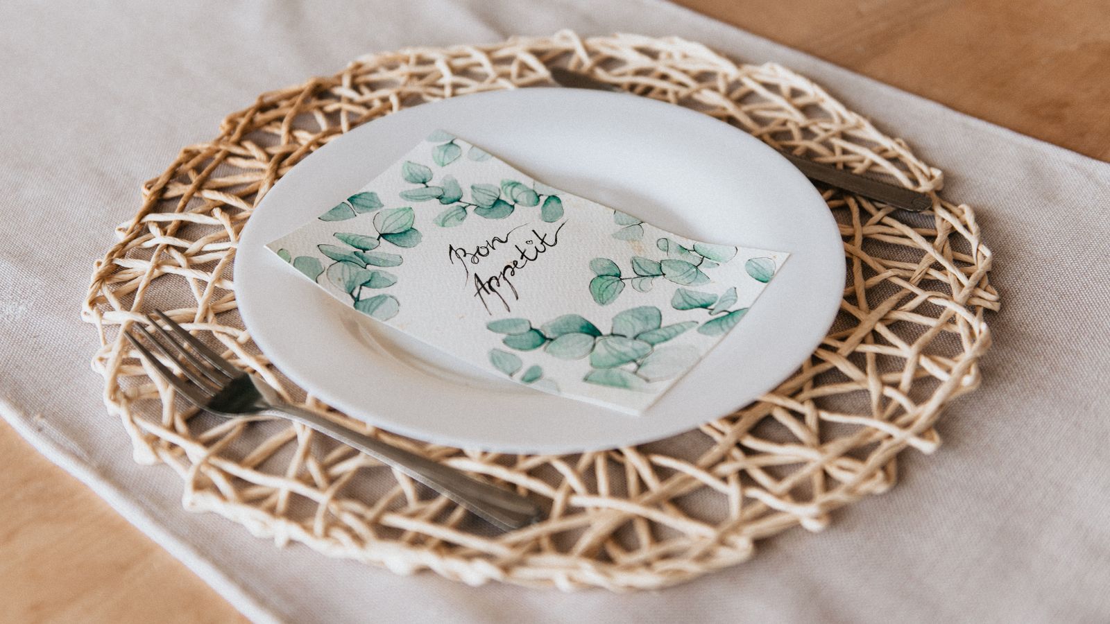 Close-up of a stylish table setting with cutlery and woven placemat on a wooden table