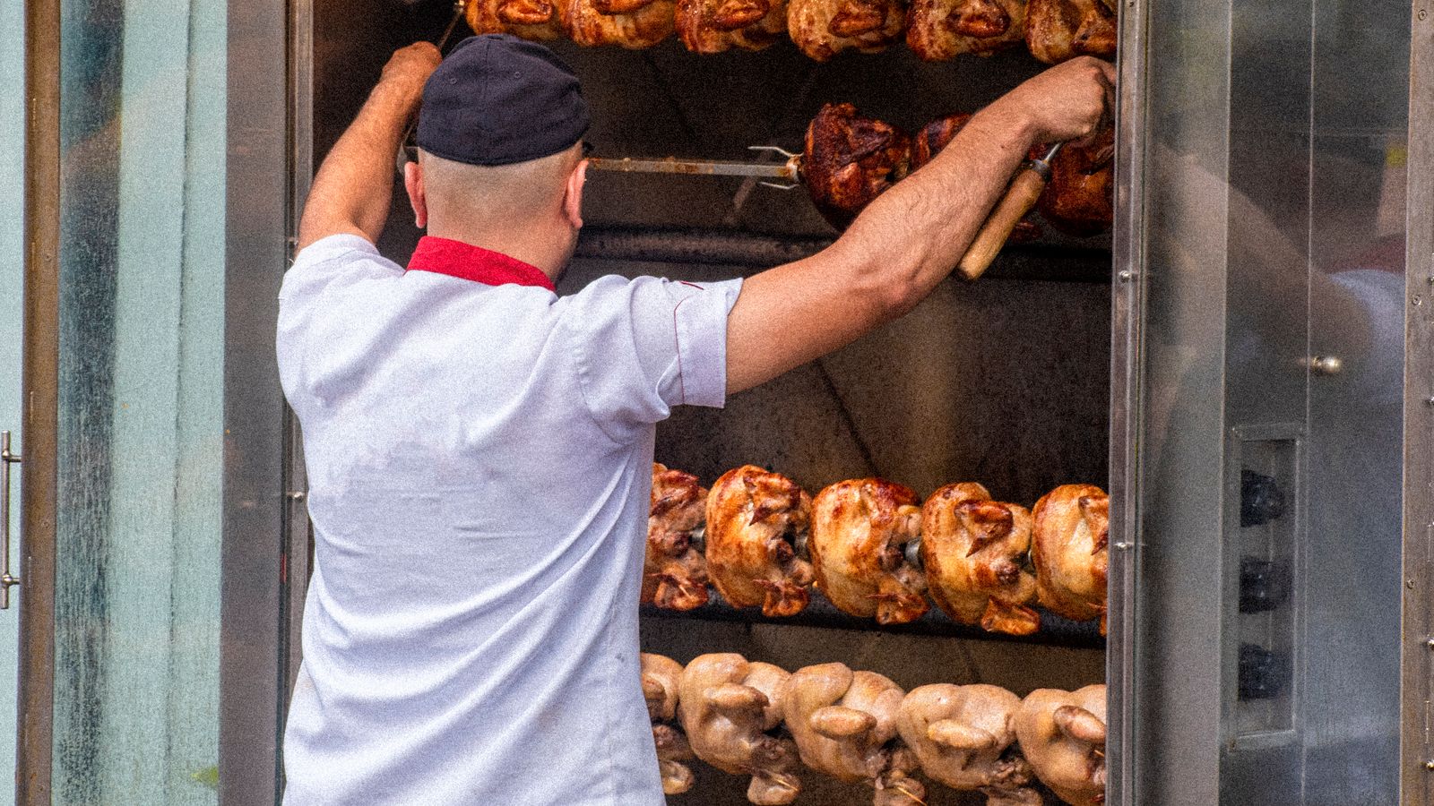 Whole chicken roasting on a rotisserie spit over an outdoor grill