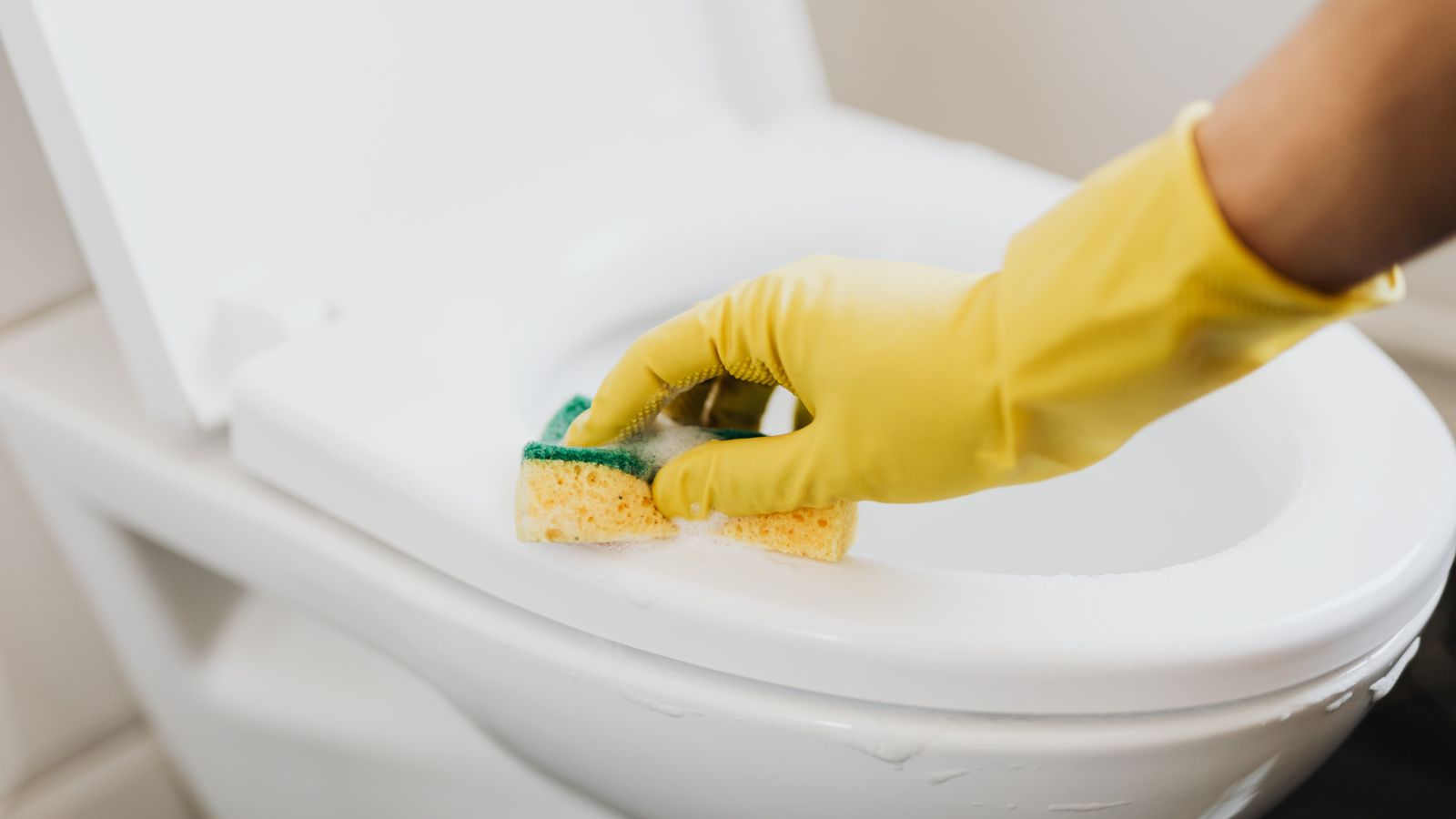 Yellow-gloved hand scrubbing a toilet bowl with a cleaning brush and cleaner