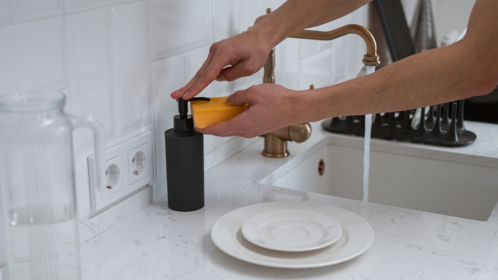 Person wearing rubber gloves scrubbing a stainless steel bar sink basin