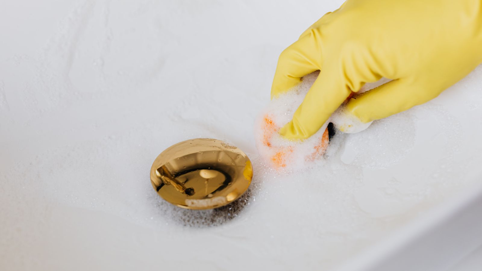 Person scrubbing a kitchen sink drain flange with a brush during a deep clean