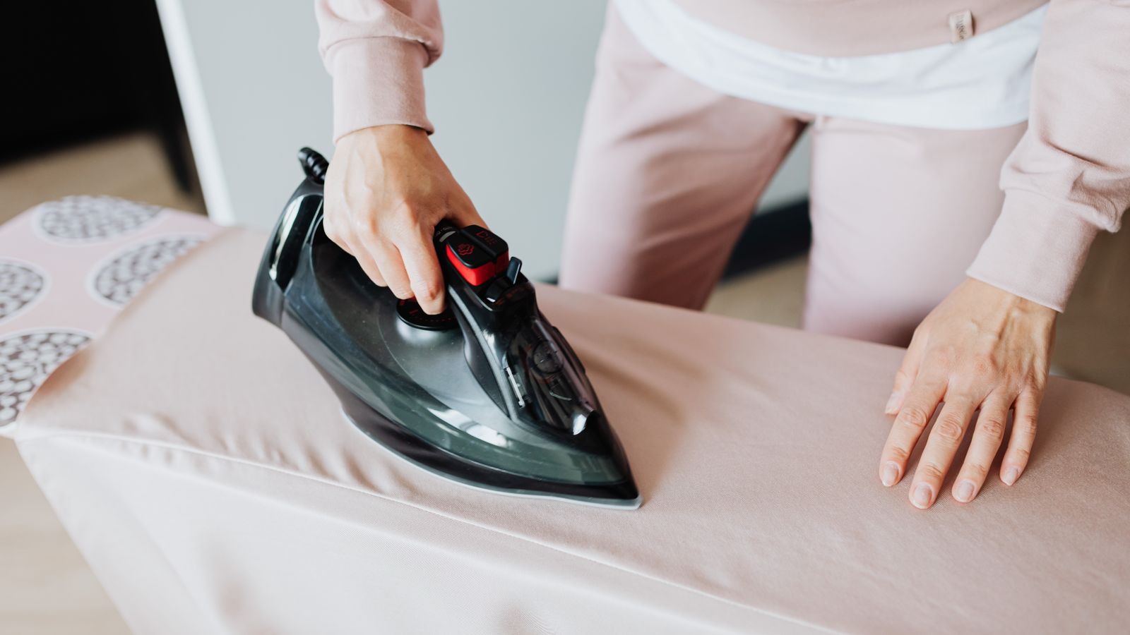 Close-up of hands cleaning an ironing board cover with a cloth and spray bottle