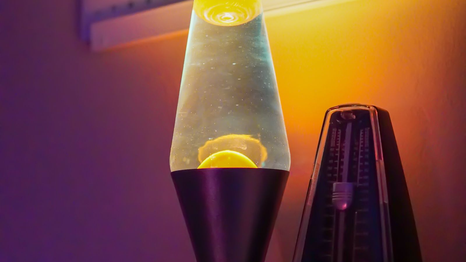 A glowing lava lamp beside a lit candle on a dark wooden shelf