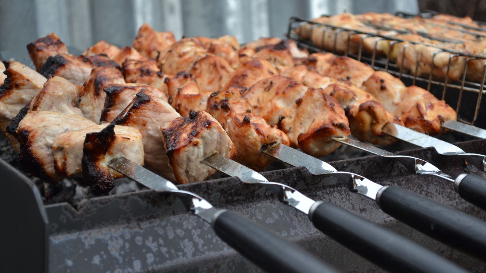 Assorted meat and vegetable skewers ready for grilling next to griddle tools