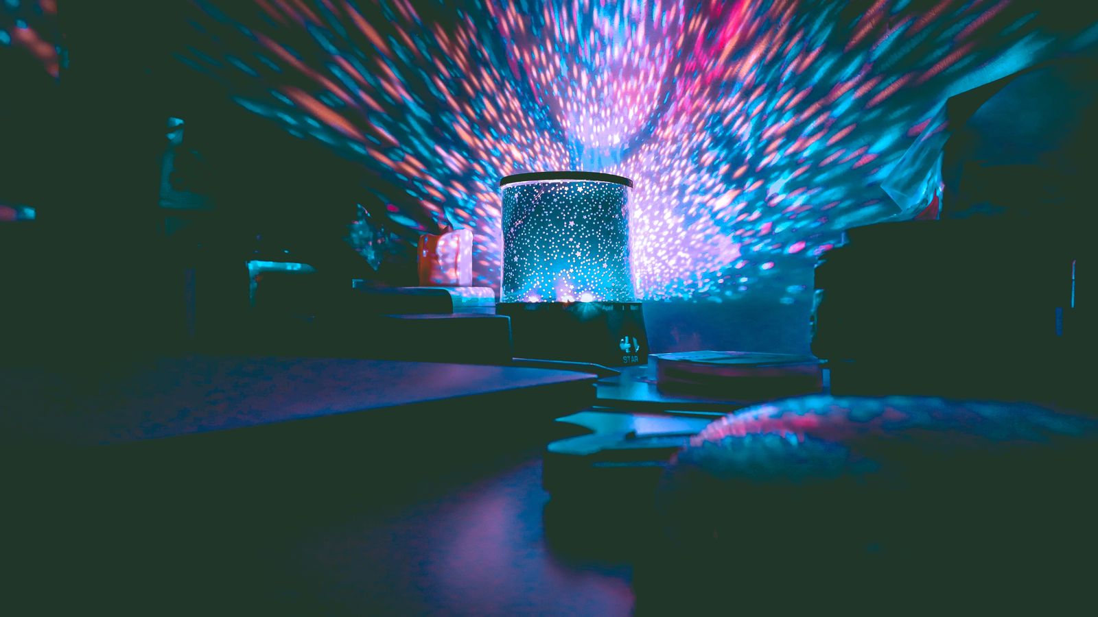 Star projector casting colorful galaxy light patterns across a dark bedroom ceiling