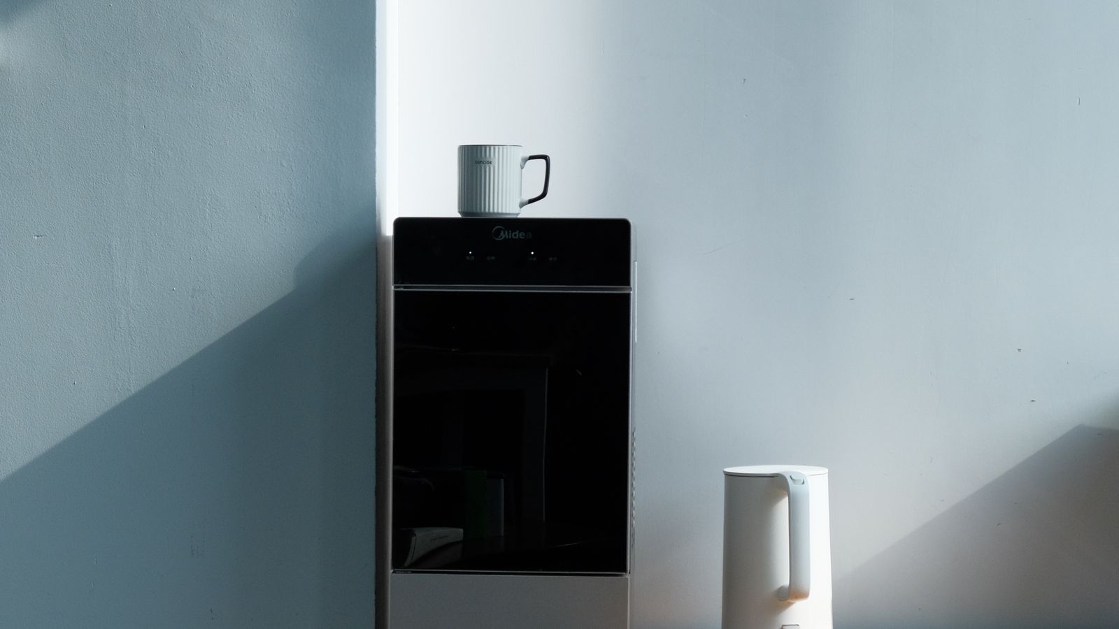 Person pouring near-boiling water from an instant dispenser into a mug in a small kitchen