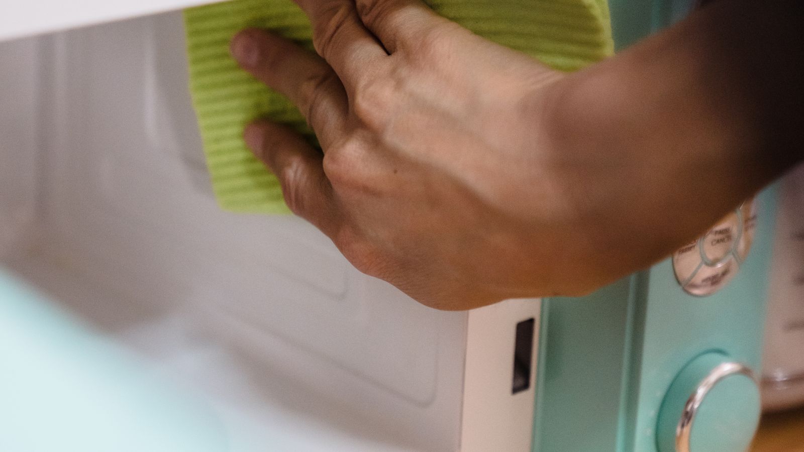 Person cleaning kitchen appliance surface with a wipe while wearing gloves