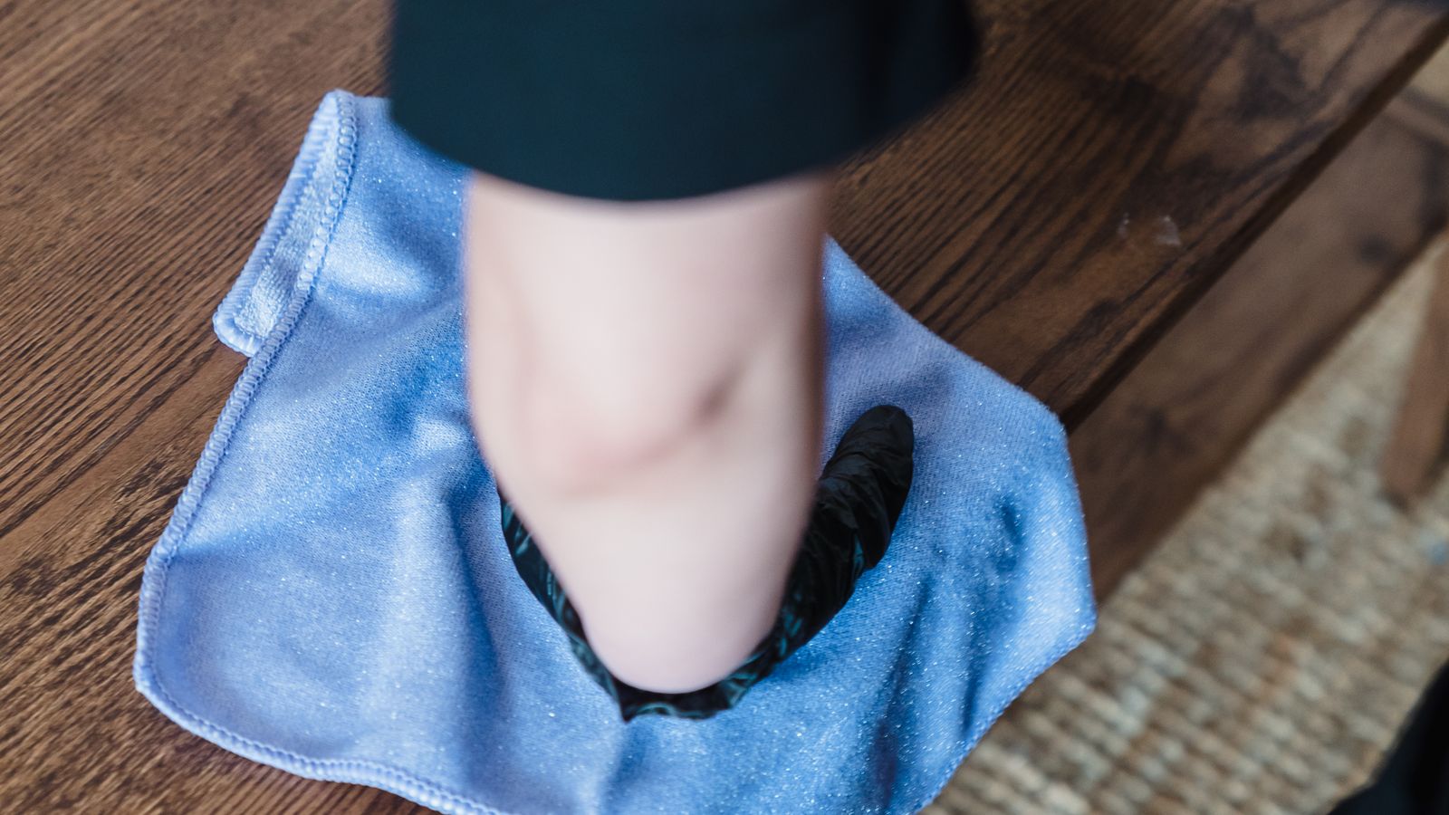 Person wiping a wooden dining table with a microfiber cloth and cleaning spray