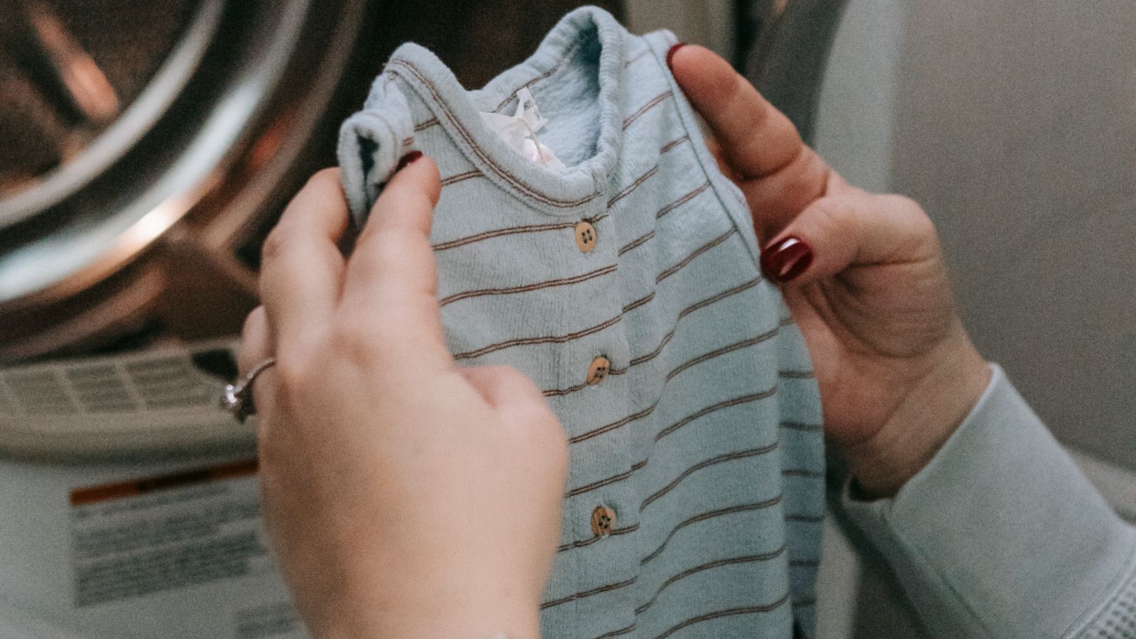 Parent sorting baby clothes near a washing machine with a gentle laundry detergent bottle nearby