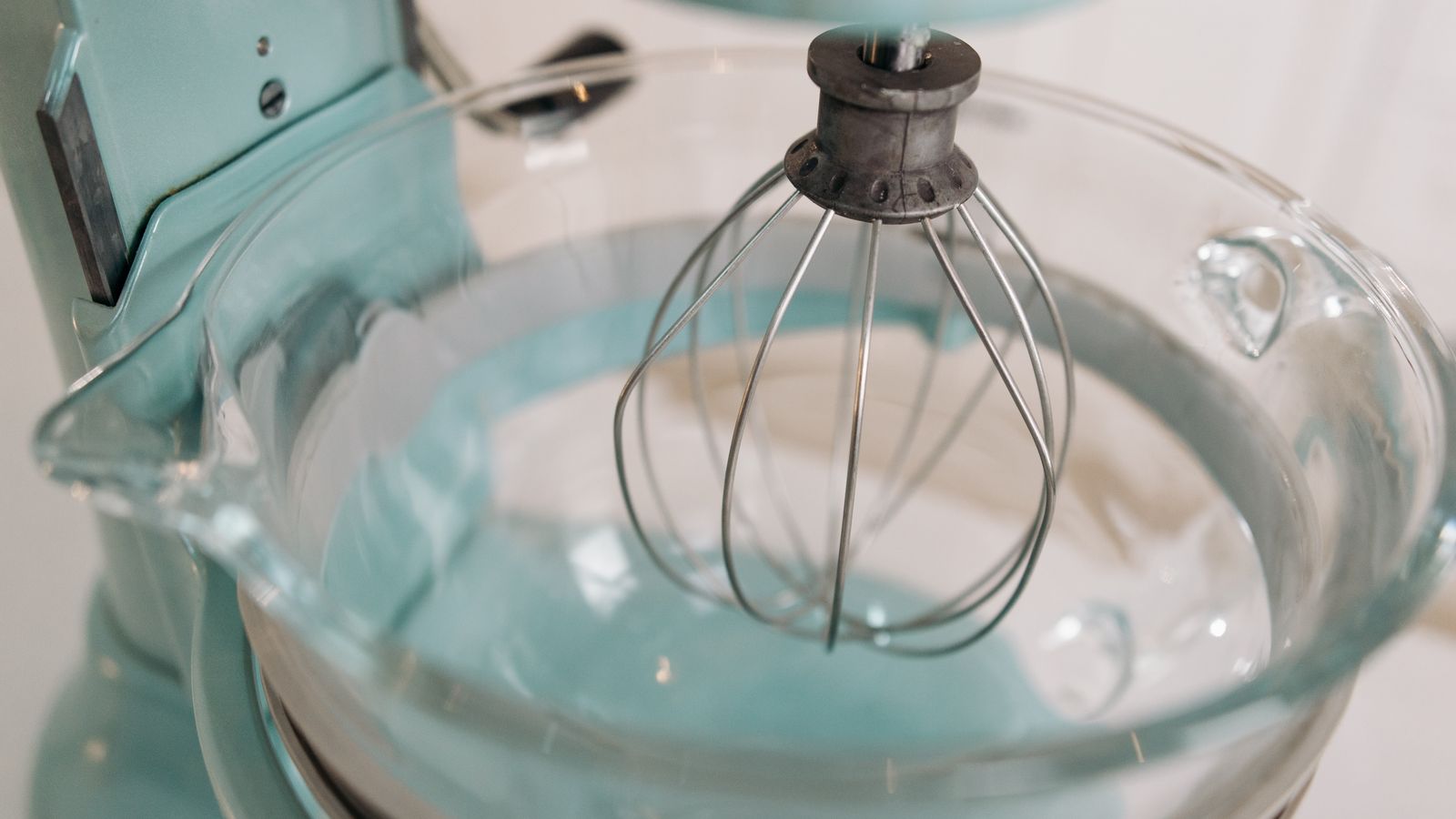 Turquoise stand mixer with whisk attachment on a tidy kitchen counter