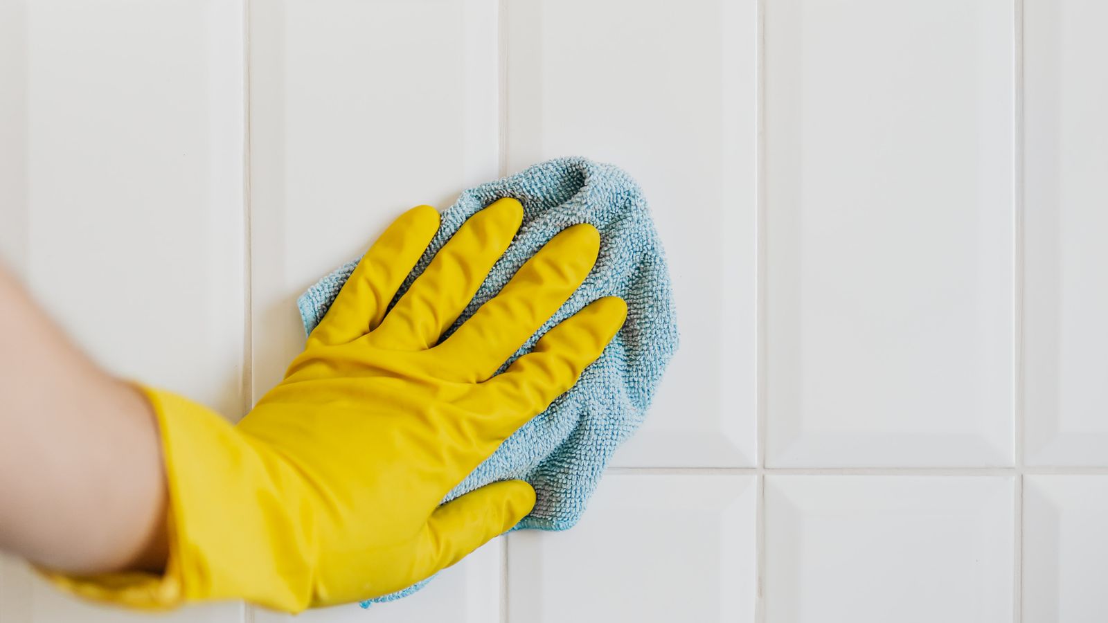 Person mopping a tiled floor with a bucket of cleaning solution nearby