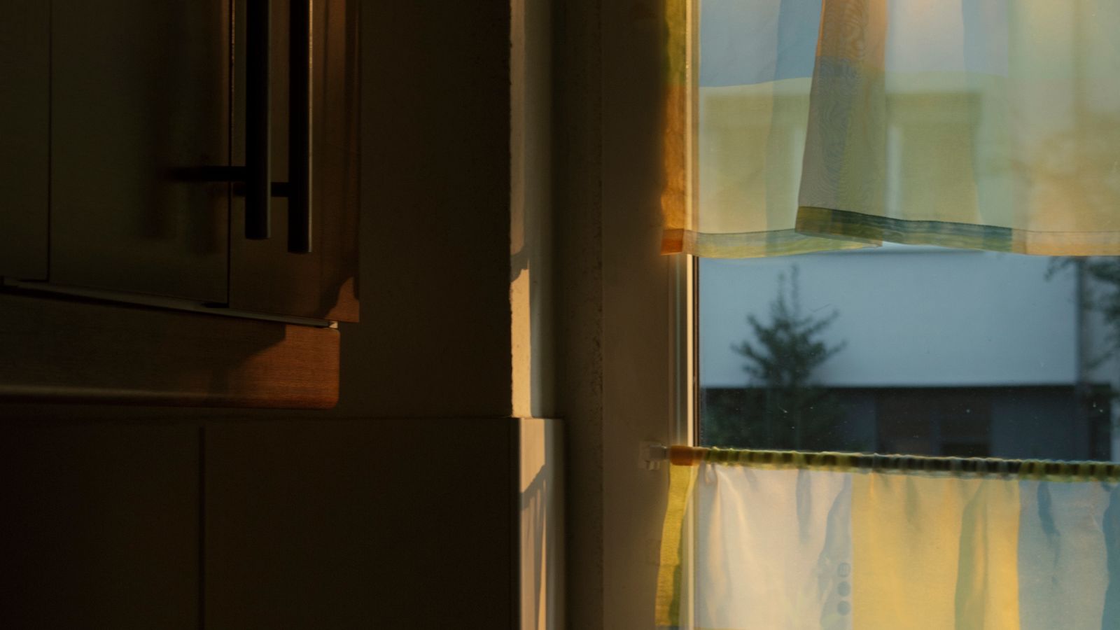 Light kitchen curtains hanging beside a sunny window above a sink