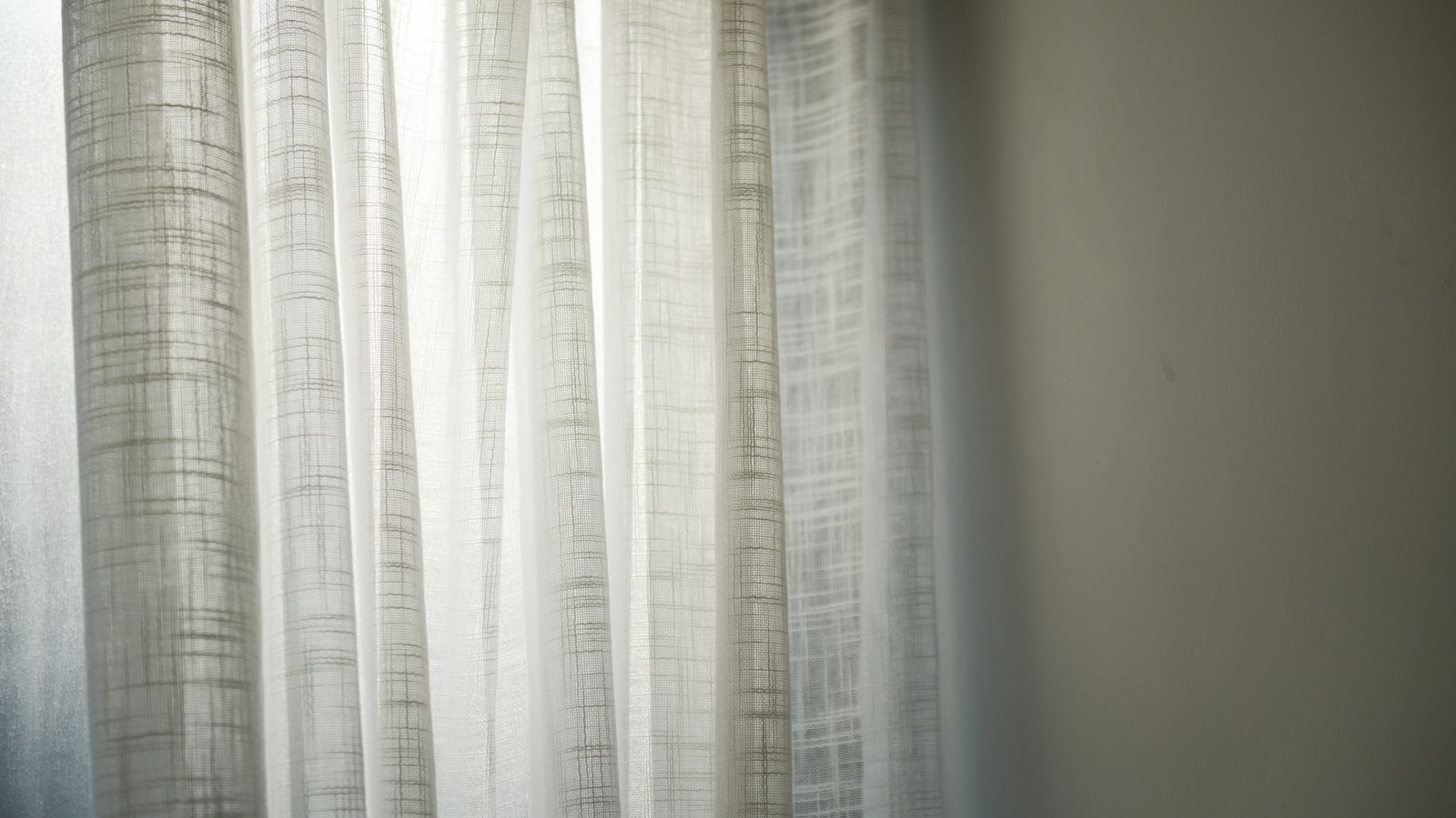 Close-up of sheer curtain fabric texture hanging near a bright window