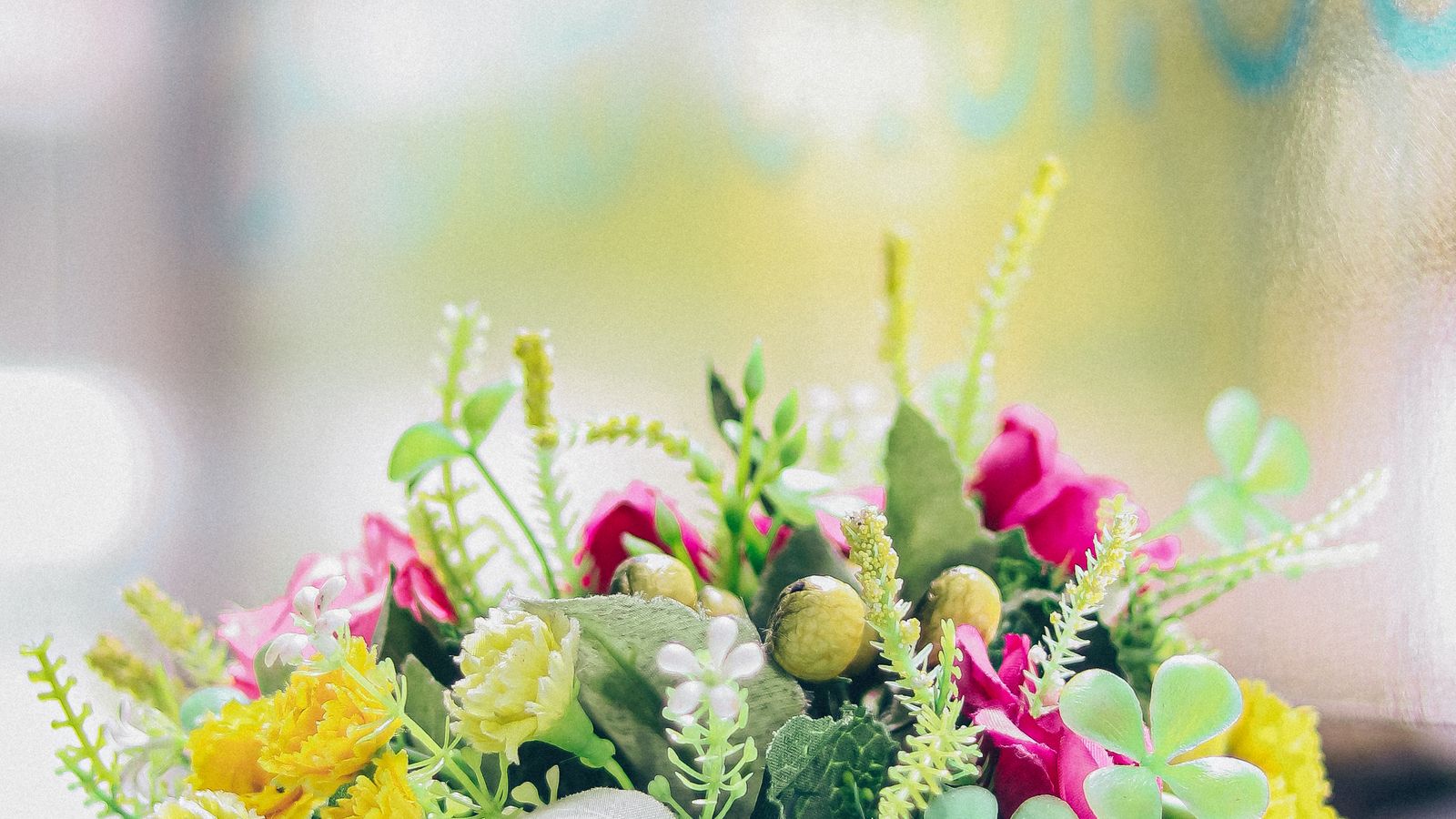 Bright artificial flower arrangement in a white vase styled on a sunlit table