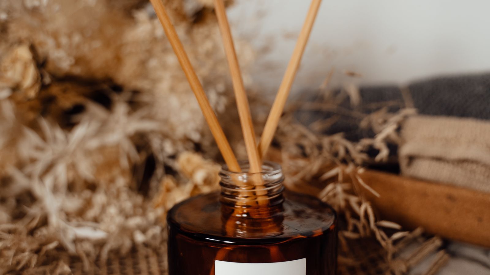 Minimalist reed diffuser in a glass jar with reed sticks releasing fragrance in a living room
